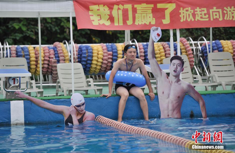 一市民坐在中国游泳运动员的照片旁。 陈超 摄 8月10日,重庆洋人街一游泳池挂起孙杨、宁泽涛等中国游泳名将的照片,鼓励前来游泳健身的市民向游泳冠军学习。图为游泳池挂起孙杨、宁泽涛等中国游泳队运动员的照片。陈超摄